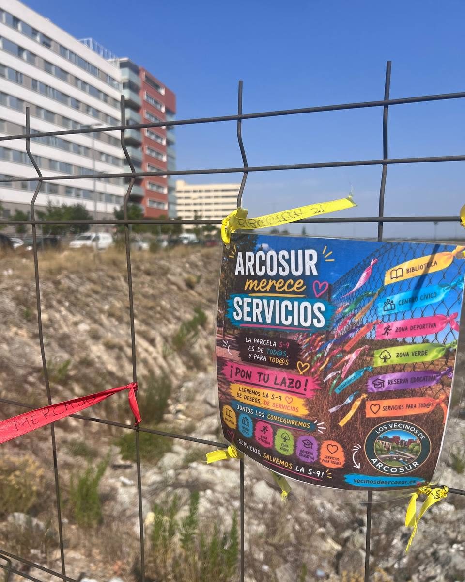 Cartel de la campaña Arcosur merece servicios atado a la valla, con los bloques del barrio detrás