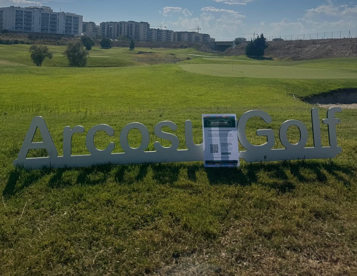 El cartel de apoyo a los vecinos de Arcosur, junto al rótulo de Arcosur Golf, con el campo y los bloques de viviendas del barrio al fondo