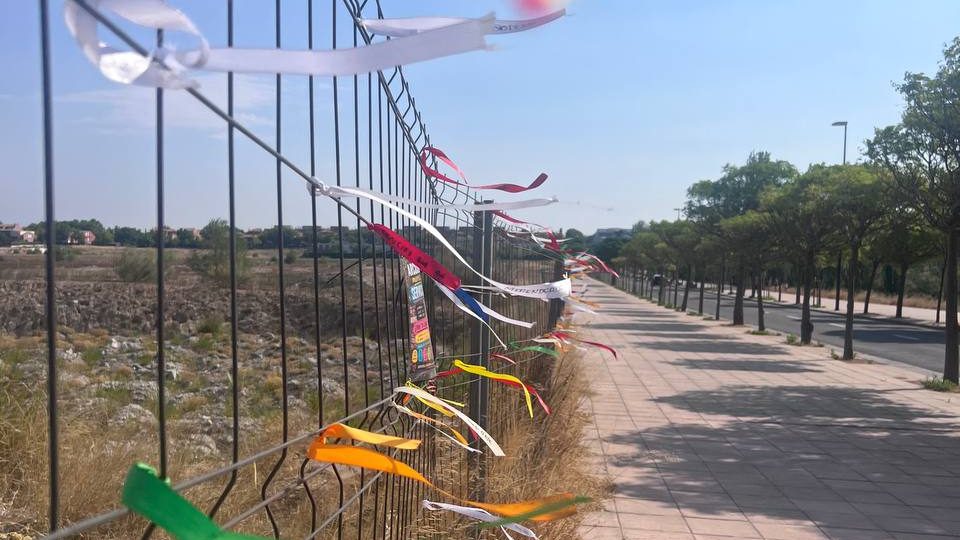 Panorámica de la valla de la parcela S-9 cubierta de lazos, junto a los bloques del barrio